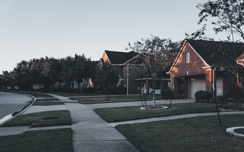 Suburban street of brick houses with landscaped lawns at dusk.